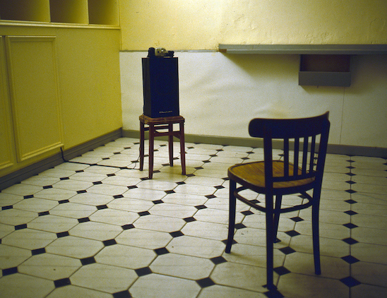 Past Conversation (1997) variable dimensions. Found objects (chair, stool) speaker, headphones, hardware, audio (Installation in former bookmakers, Chamberlain Street, Derry)